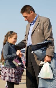 Father holding his daughter's hand while carrying belongings, suggesting shared custody or visitation exchange.